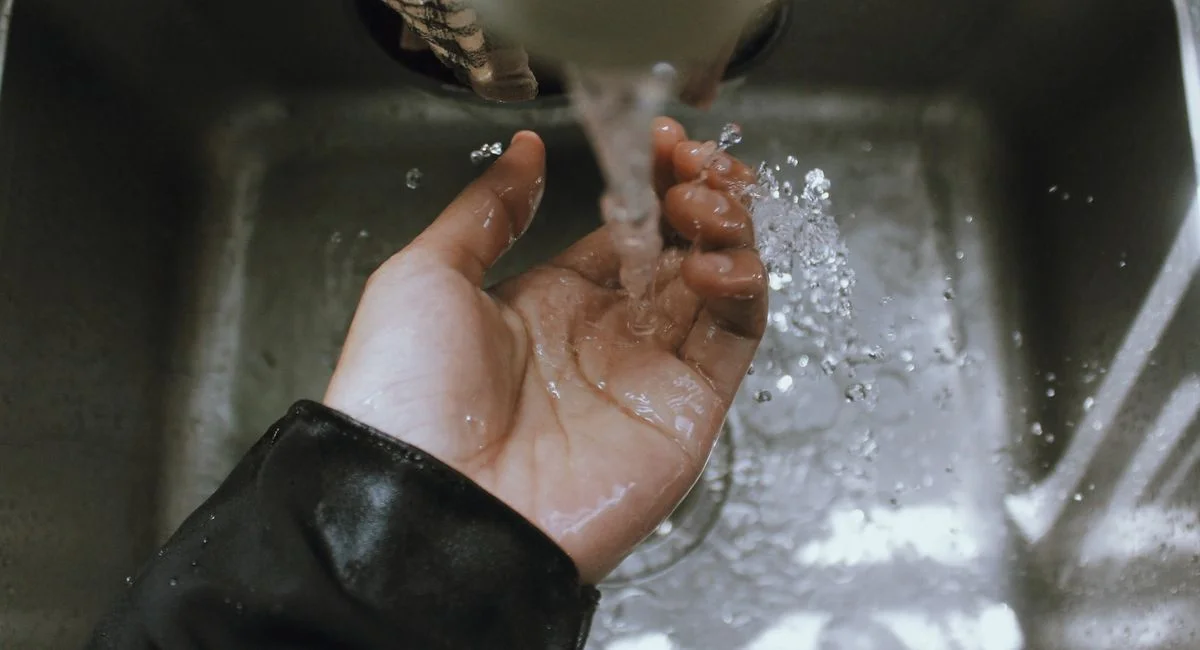 Close-up of a hand being washed under a stream of running water in a sink, emphasizing cleanliness.