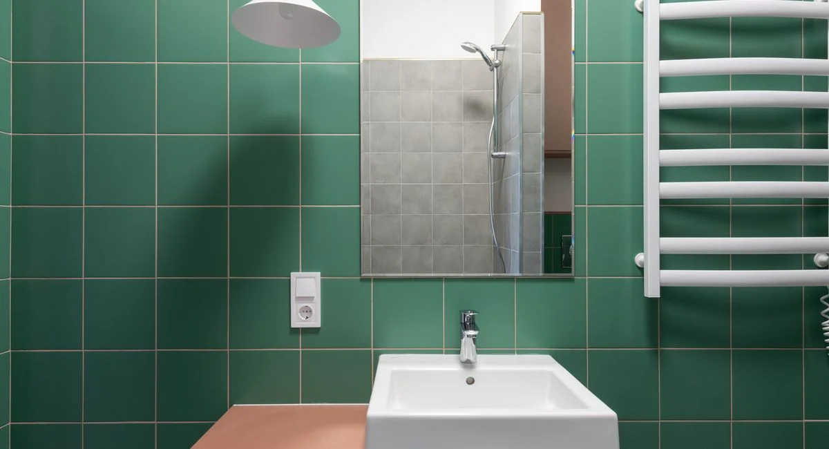 Modern bathroom with green tiled walls and white ceramic sink under mirror reflecting shower designed in minimal style