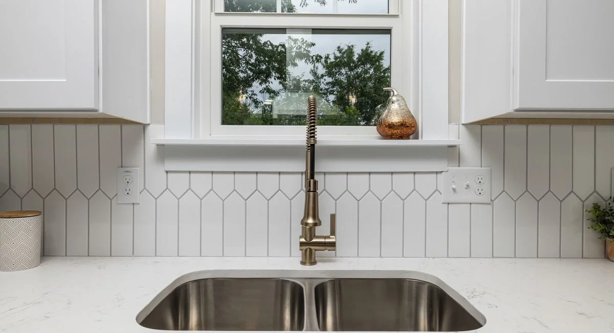 Contemporary kitchen design featuring white cabinets and a stainless steel sink with a minimalist faucet.