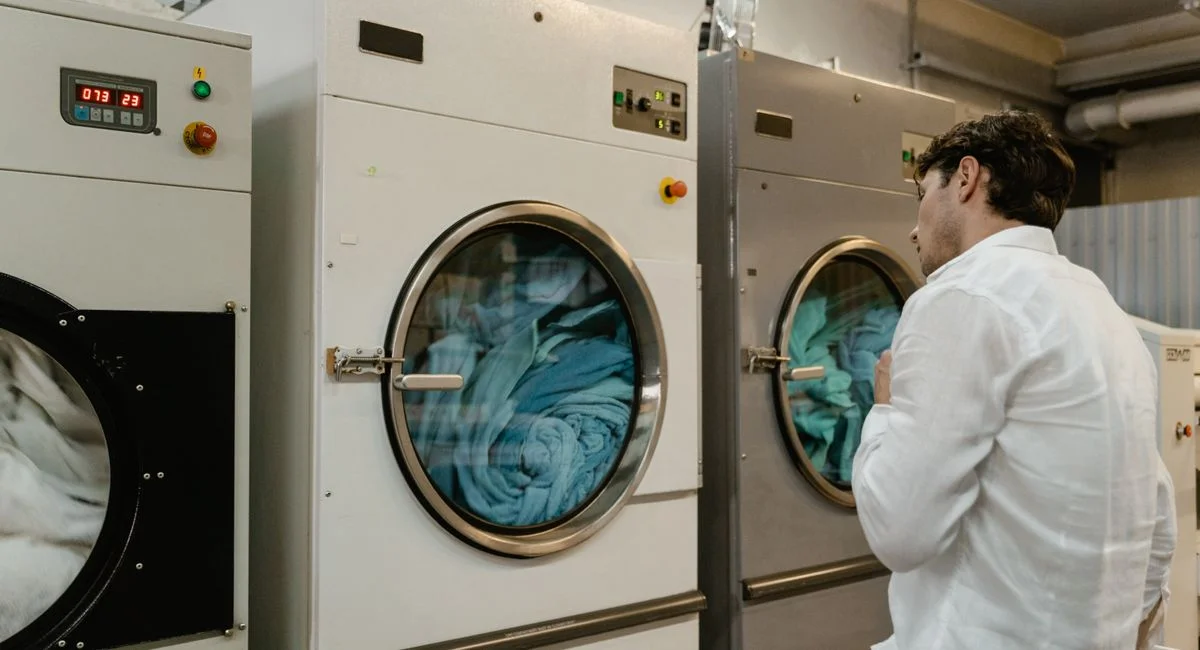 A man wearing a white shirt uses industrial washing machines in a public launderette.
