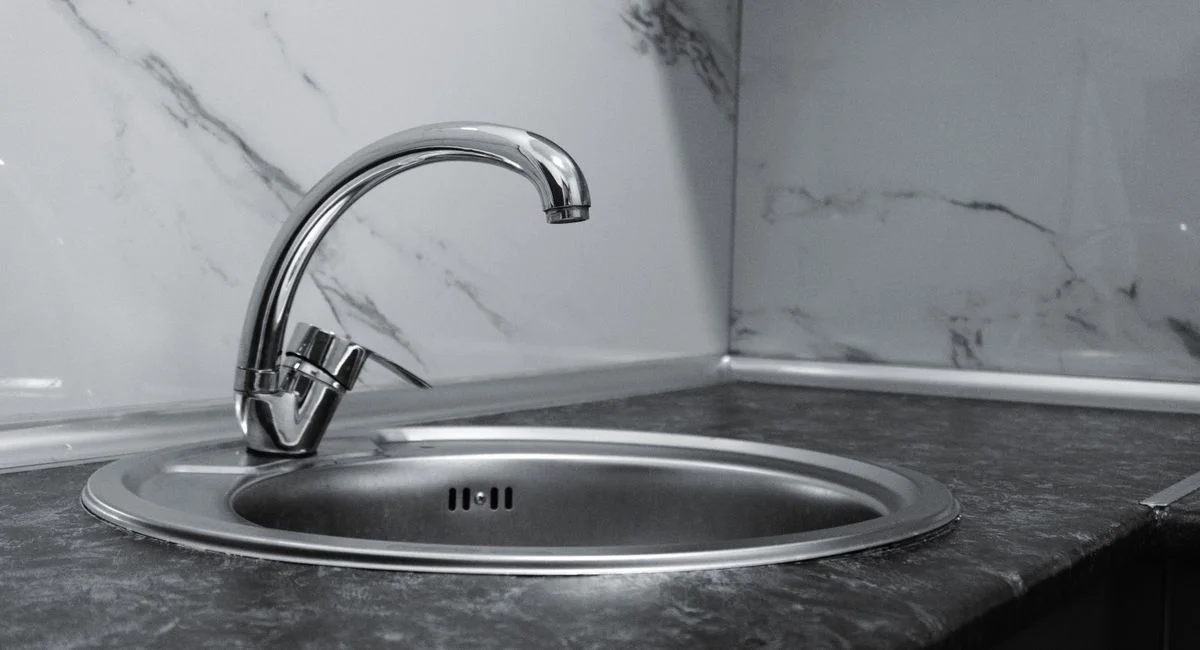 Stainless steel kitchen sink and faucet against marble backsplash in a modern kitchen.