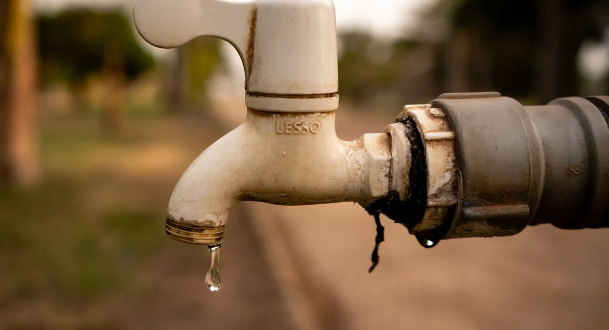 A close-up shot of a water droplet falling from an outdoor tap, highlighting water conservation issues.