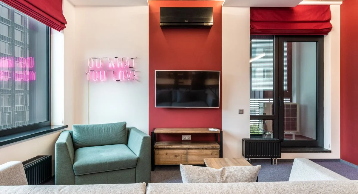 Interior of modern office lounge zone with sofa and armchair with table near window next to TV on wall and neon signboard wit