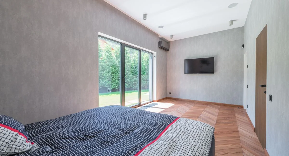 Bright and cozy minimalist bedroom with large sliding glass doors and wooden flooring.