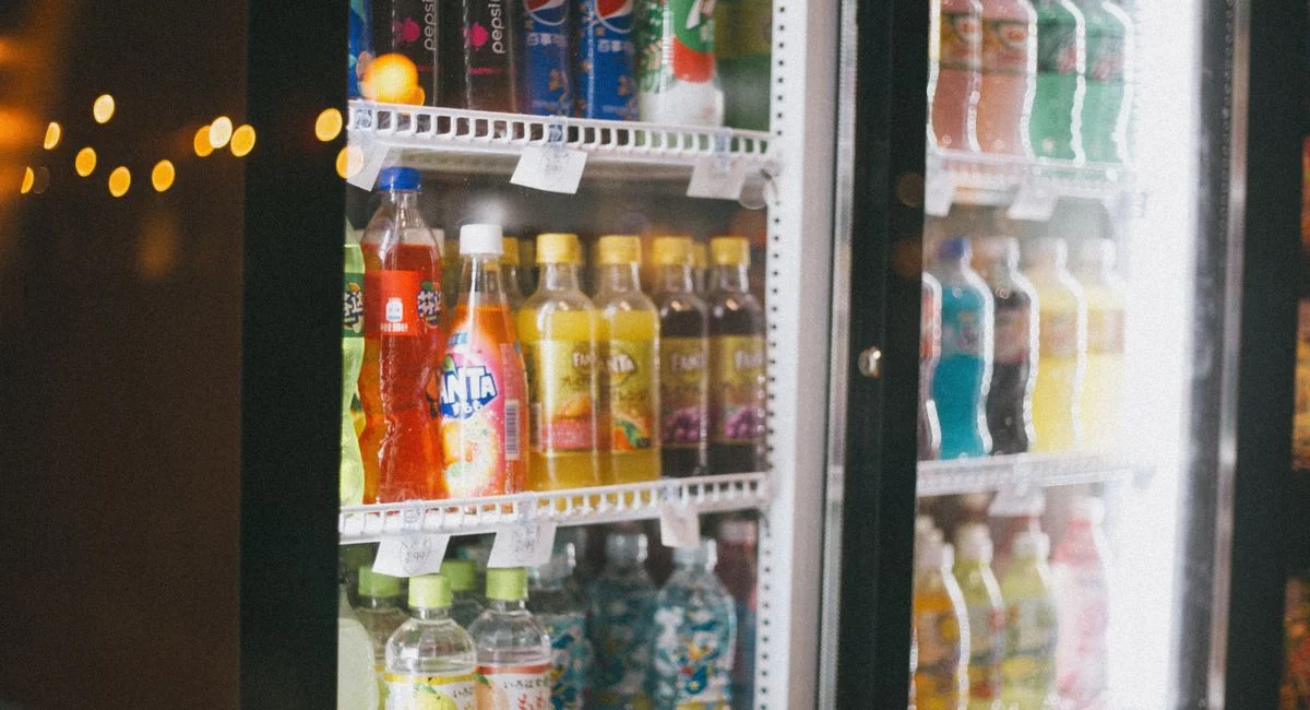 Assorted bottles of soft drinks in a commercial refrigerator with glass doors.