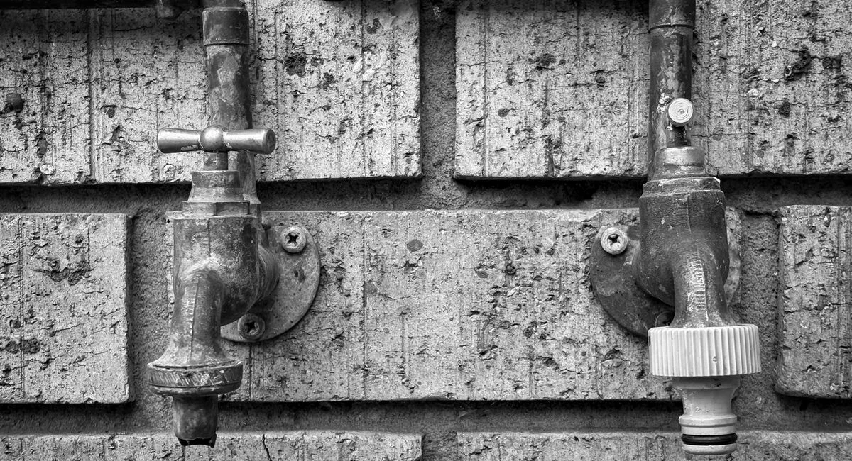 Close-up of vintage outdoor plumbing taps on a brick wall, black and white.