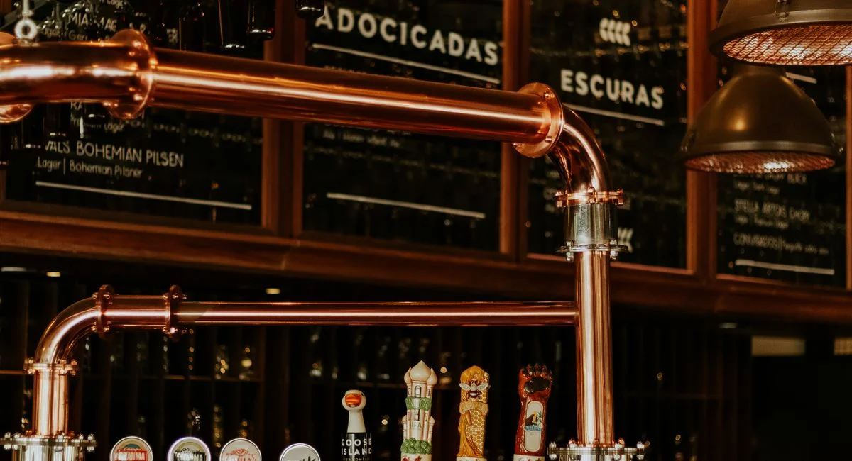 Close-up of a brewery taproom interior featuring copper pipes and beer taps. Ideal for beverage industry visuals.