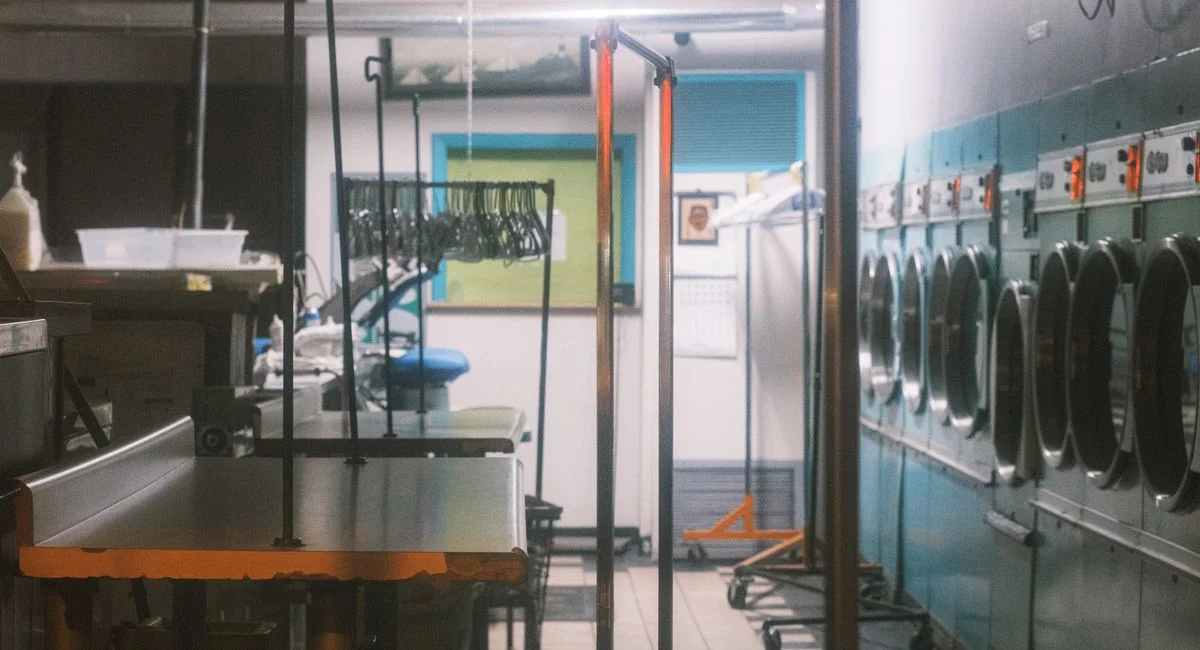 Interior view of a commercial laundry facility with machines and clothing racks.
