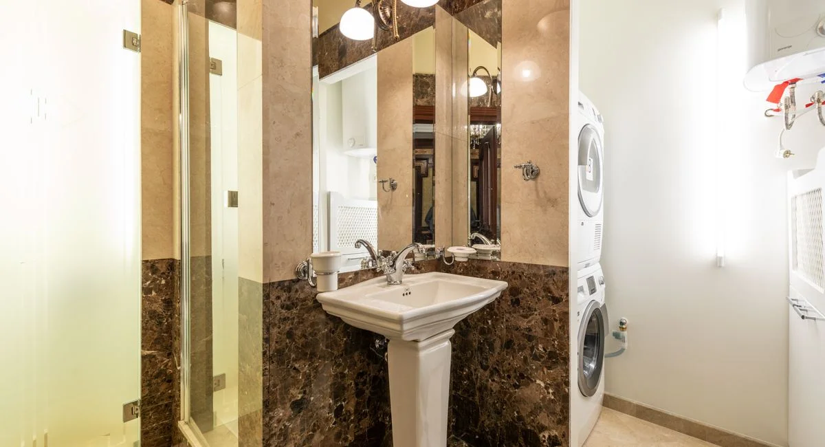 Elegant bathroom interior featuring marble walls, a pedestal sink, and a washer-dryer unit.