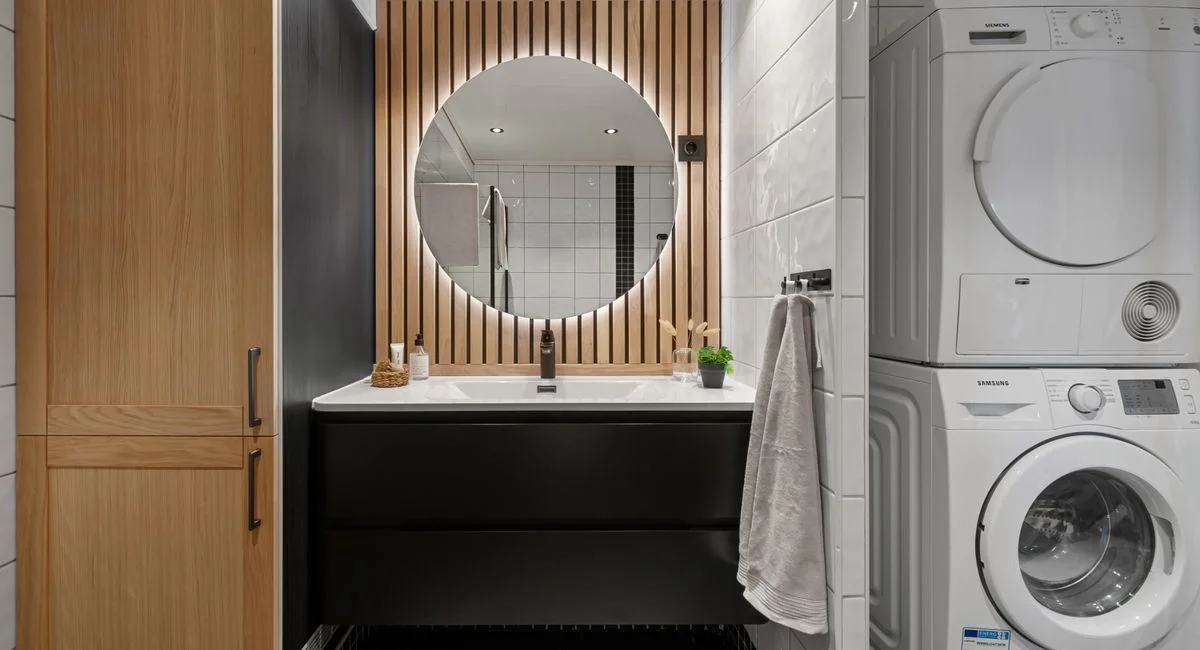 Sleek bathroom featuring a round mirror, modern sink, and integrated washer and dryer.